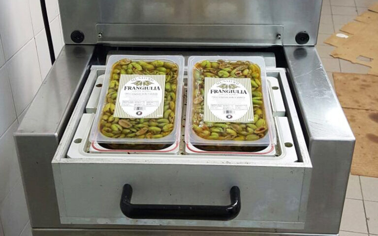 Packaged olive containers moving through a sealing machine, demonstrating the brand system applied in production and packaging operations.
